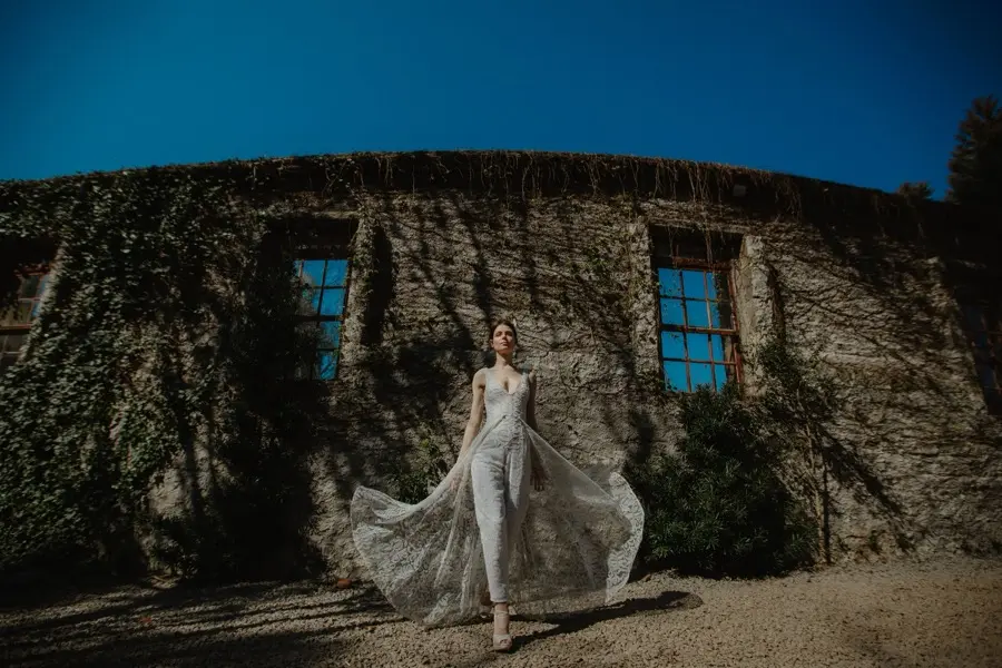 A person in a flowing dress walking outside an ivy-covered stone building